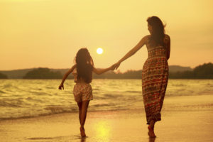 Mother and daughter walking on the beach with sunset